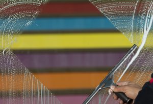 Rainbow stripes on a wall framed by a window squeegee wiping the soap away for a clearer view.